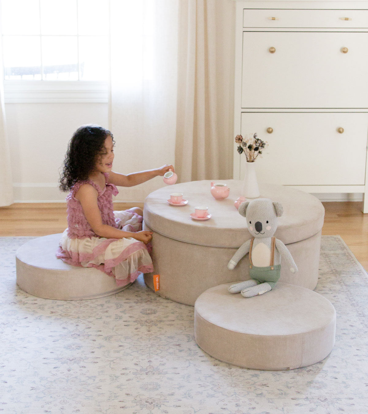 A child hosts a playful tea party on a beige Chunk™ play ottoman, set up as a cute playroom table.