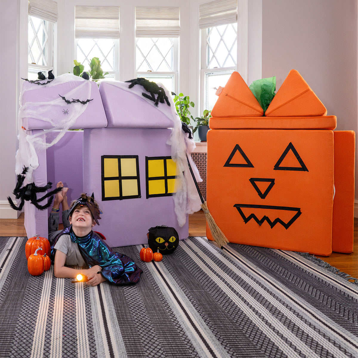 A child in costume plays inside two forts made from a lilac purple Nugget and an orange Nugget.