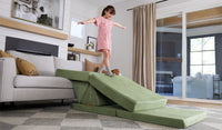 A child balances on a Bamboo mossy sage Nugget play couch, set up as a ramp onto the conventional family couch.