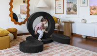A child crawls through the hoop of a Catwalk all-black Chunk play ottoman.