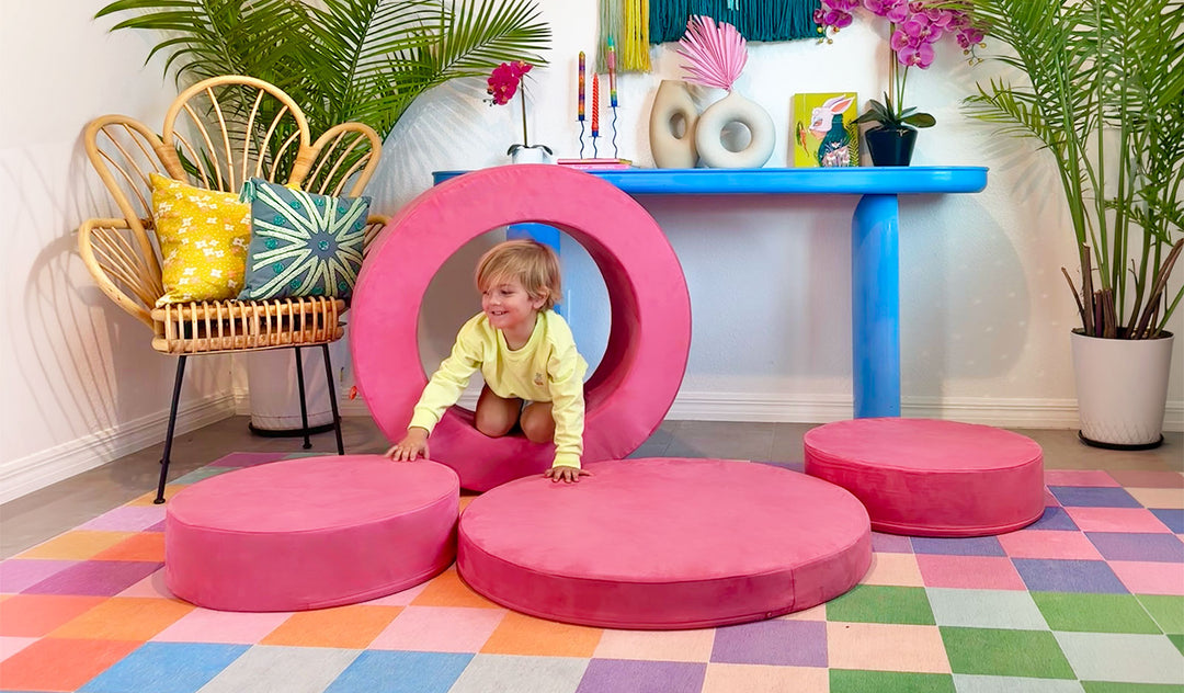 A child climbs through the hoop of a hot pink Popstar Chunk play ottoman.