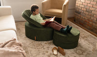 A child reads a book in a Willow forest green Chunk play ottoman, set up in a chair configuration.