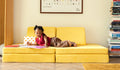 A young child reads a book on a Lemonade classic yellow play couch by Nugget.