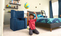 A child tosses a ball backwards into a basket built from the three pieces of a navy blue Smore play chair.