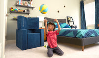 A child tosses a ball backwards into a basket built from the three pieces of a navy blue Smore play chair.
