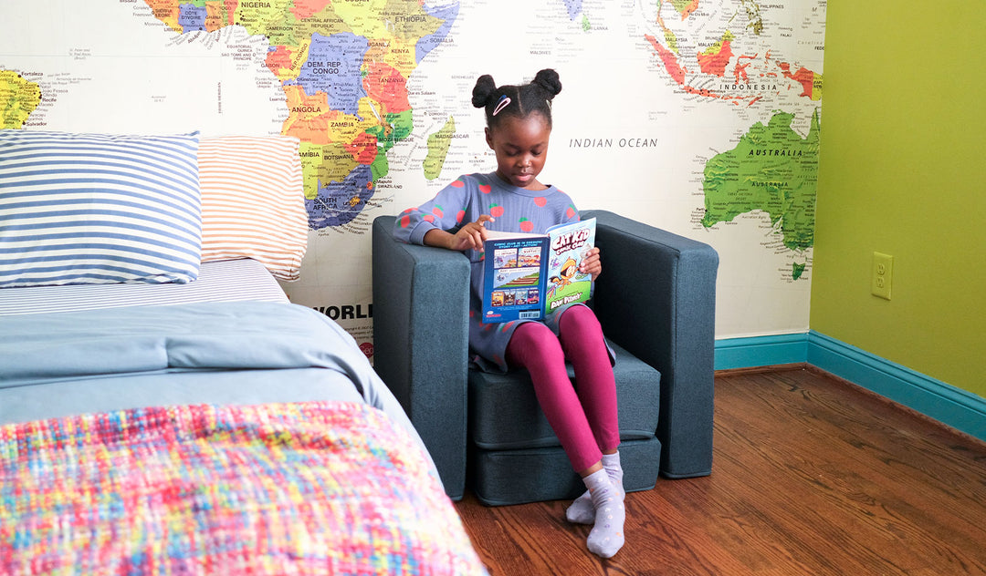A child reads a book in a bedroom while seated on a denim blue Smore play chair.