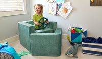 A child pretends to pilot a boat made from the three pieces of a sea green Smore play chair.