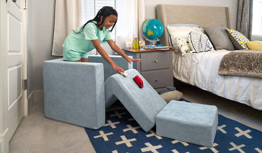 A child races toy cars down the pieces of a light gray-blue Smore play chair.