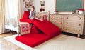 A child plays on an all-red play couch by Nugget, set up as a slide down from the child's bed.