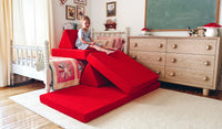 A child plays on an all-red play couch by Nugget, set up as a slide down from the child's bed.