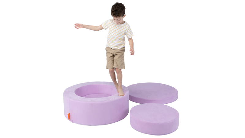 A child balances on the edge of a light purple play ottoman, designed for functional use and imaginative play.