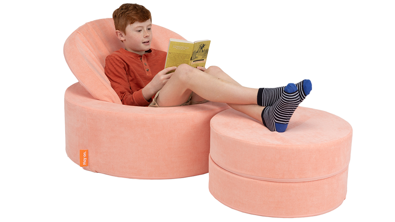 A child reads a book inside a peach-colored play ottoman, set up like a comfy seat for the playroom.