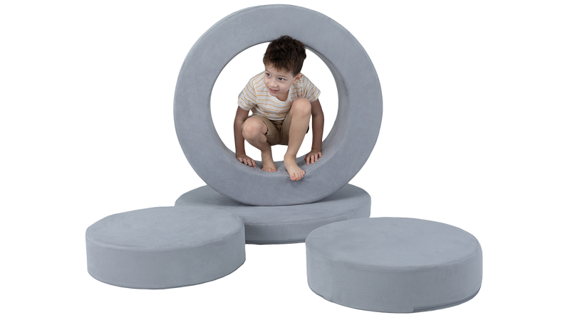A child plays inside the hoop of a light gray storage ottoman, disassembled for imaginative play.