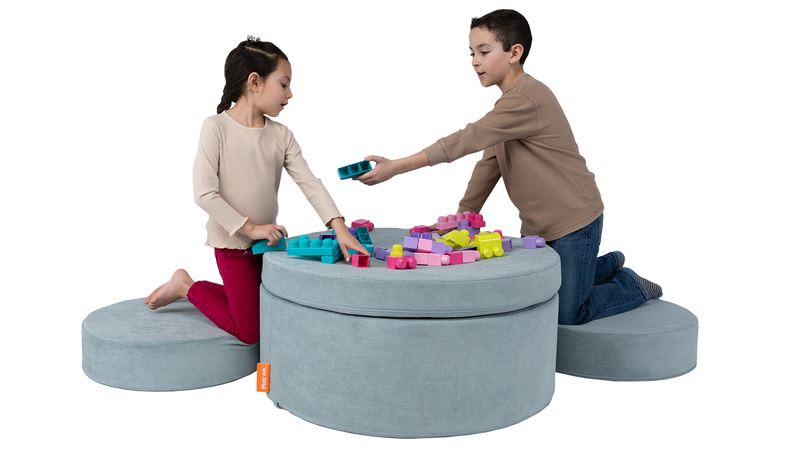 Two children play with toys on top of a light blue, round play ottoman, set up as a playroom table and chairs.