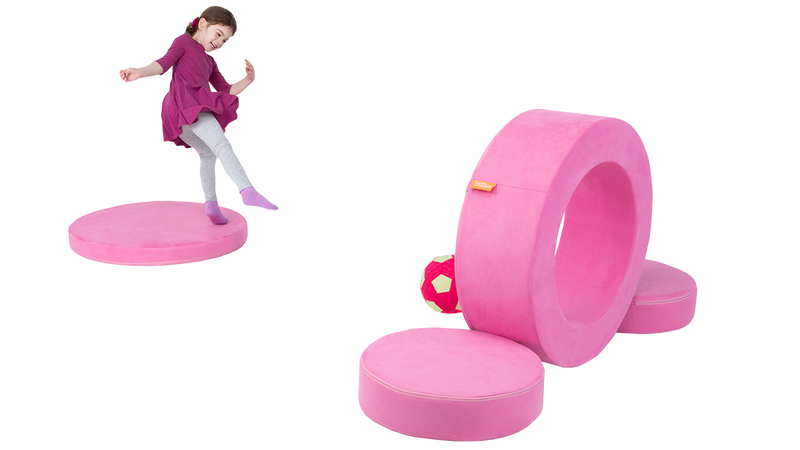 A child takes aim at a target made from the hoop of a candy pink storage ottoman, designed for imaginative play.