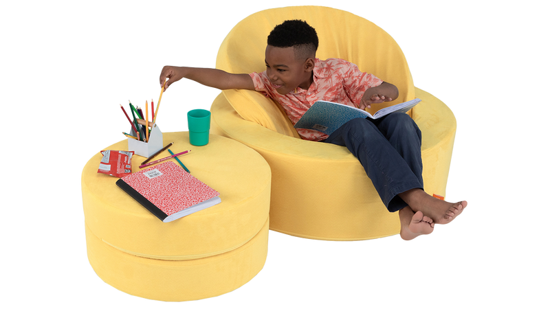 A child does artwork while seated in a yellow storage ottoman, using the foam pieces as a playroom side table.
