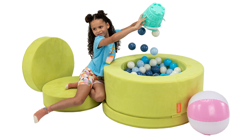 A child plays in a chartreuse storage ottoman, fashioning it into a ball pit for imaginative play.