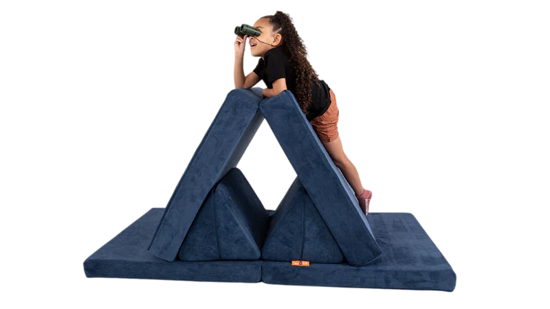 A child looks through binoculars from the summit of her Nugget mountain build, made with a navy blue play couch.