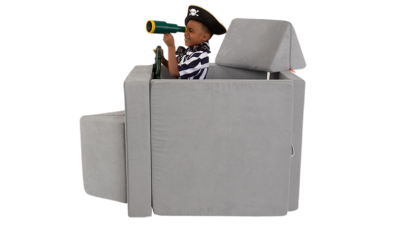 A child looks through a telescope as he plays on a pirate ship build, made from a light gray Nugget play couch.