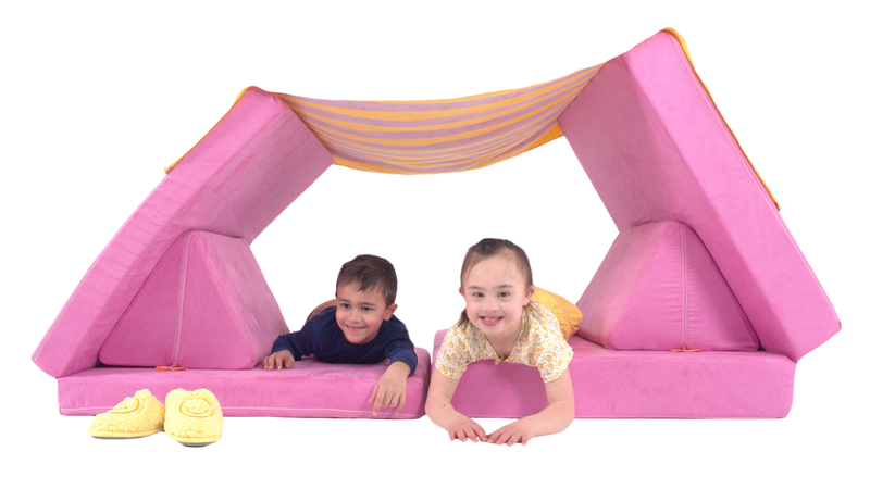 Two children smile and play inside a Nugget fort made from a pink Nugget play couch and a blanket.