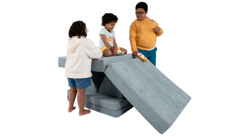 Three children race toy cars down a ramp built from one light blue Nugget play couch