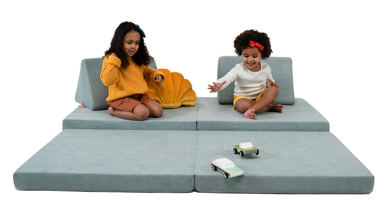 Two children race toy cars across a light blue Nugget play couch.