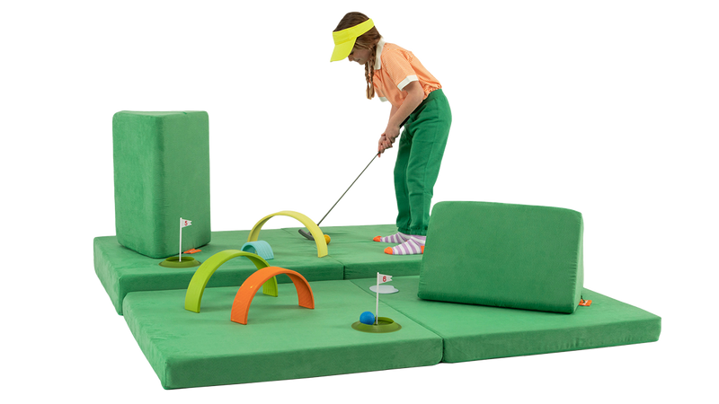 A child plays a round of mini-golf on a course built across a green Nugget play couch.