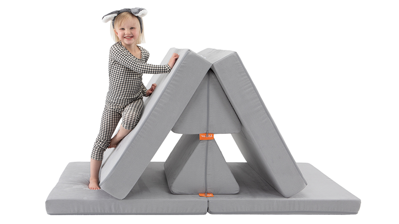 A child smiles and climbs a Nugget mountain build — created using one light gray Nugget play couch.