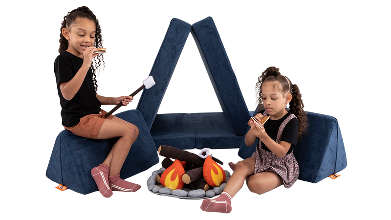 Two children pretend to eat s’mores beside a campsite build, created using a navy blue Nugget play couch.