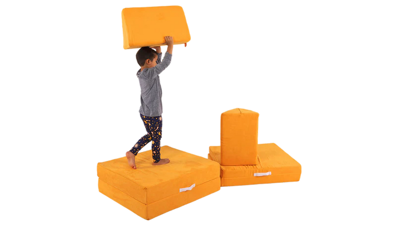 A child hoists a Nugget pillow overhead, as he walks across a Nugget stage build made with one orange play couch.