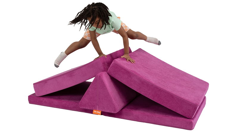 A child leaps over a one-Nugget hurdle build, made from a fuchsia Nugget play couch.