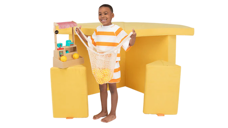 A child pretends to pick out produce at a one-Nugget farmer’s market build, made from a yellow Nugget play couch.