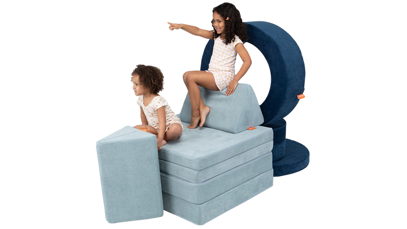 Two children engage in imaginative play with a chariot built from one Nugget play couch and one Chunk play ottoman.