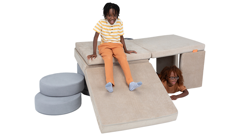 Two children crawl around and on top of a fort built from one Nugget play couch and one Chunk play ottoman.