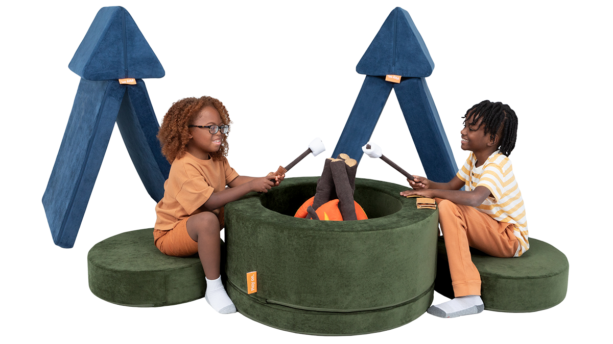 Two children play at a pretend campsite, with tents made out of a Nugget play couch, and a campfire made from a Chunk.