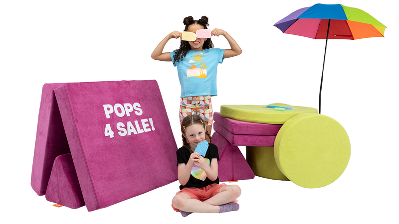 Two kids use a Nugget play couch and a Chunk play ottoman to create an imaginative stand selling popsicles.