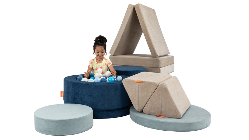 A child plays in a ball pit fort, created with two Chunk play ottomans and one Nugget play couch.
