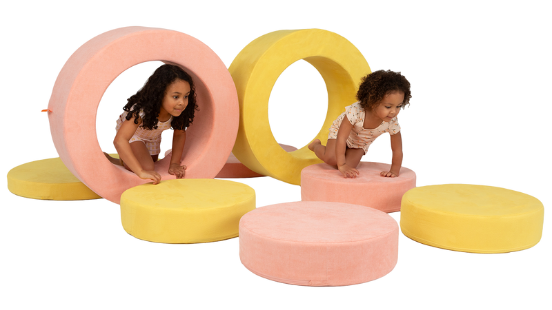 Two children crawl through an obstacle course made with the pieces of two Chunk play ottomans.