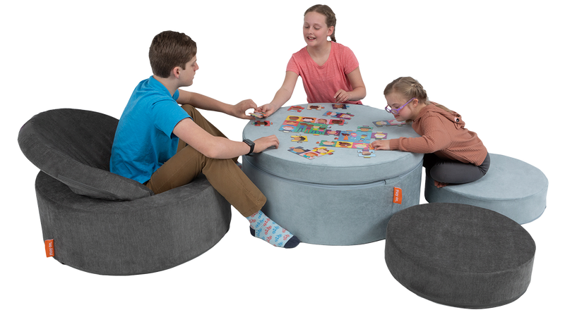 Three children work on a puzzle on a playroom table constructed with two Chunk play ottomans, using the pieces as seating.