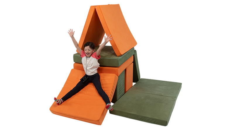 A child slides down a Nugget cushion, built into a two-Nugget fort constructed with two play couches.