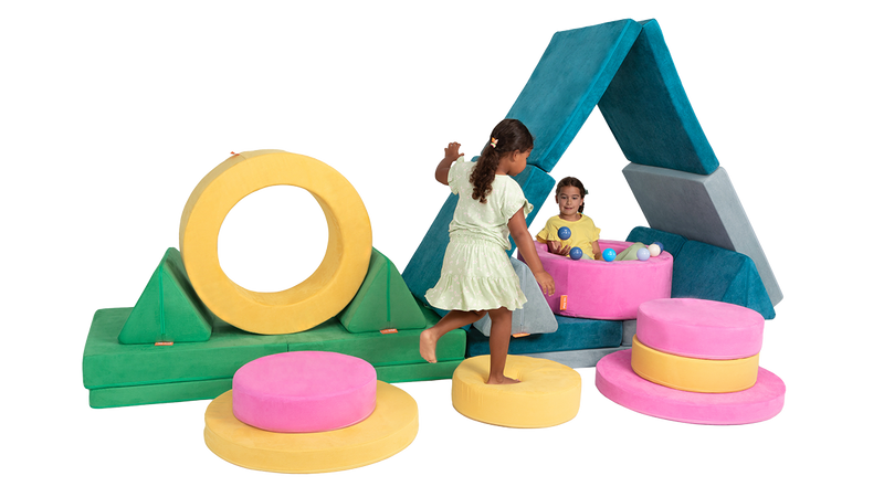 Two kids play on an elaborate play furniture build, complete with two arches, “floor is lava” stepping stones, and a ball pit.