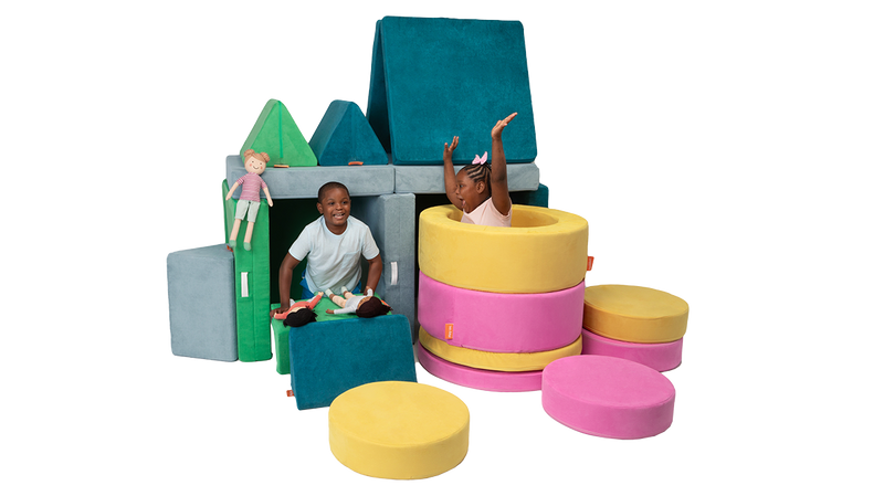Two kids play hide and seek inside an epic Nugget fort, made from two Chunk play ottomans and three Nugget play couches.