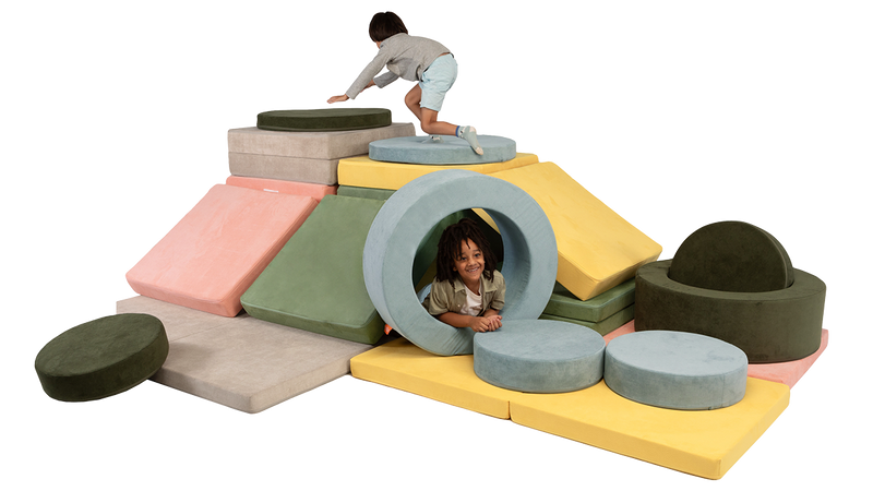 Two children engage in open-ended play with a Nugget fort made from four Nugget play couches and two Chunk play ottomans.