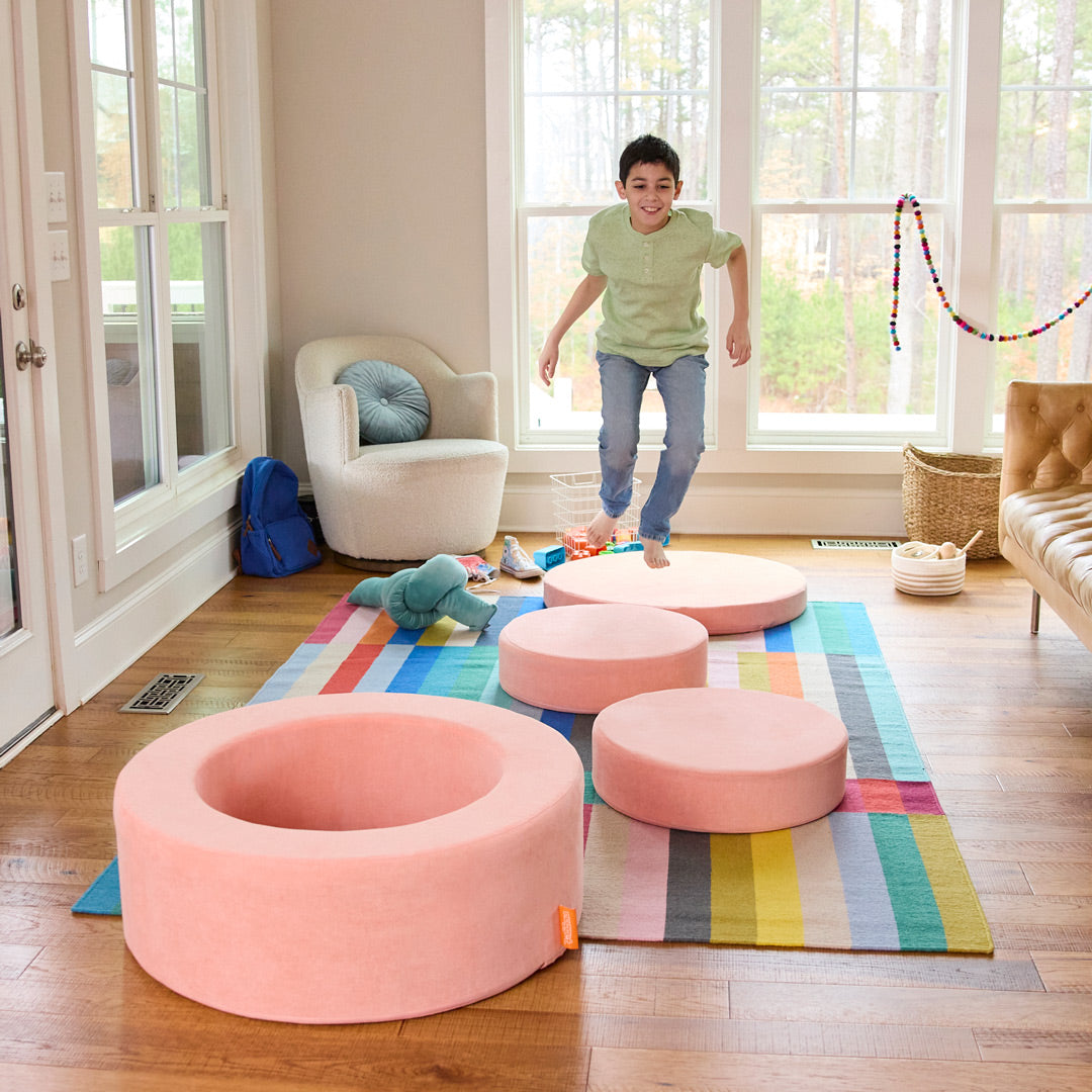 A child jumps from piece to piece on a peach-colored Nugget® Chunk™ play ottoman.