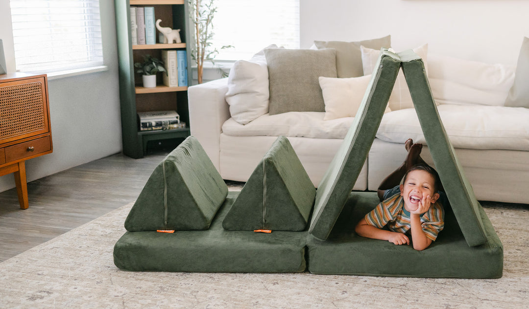 A child laughs and poses on his belly inside a tented piece of a Willow forest green play couch by Nugget.