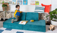 A young child reads a book on an Atlantis peacock teal play couch by Nugget, set up in a kid's sofa configuration.