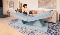 A young child pretends to surf on the balanced pieces of a Surfside light gray-blue play couch by Nugget.