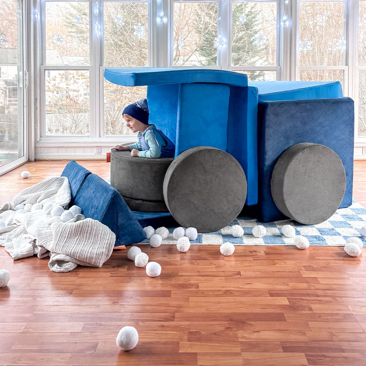 A child pretends to drive a snow plow built out of blue and gray Nugget play couches and a Chunk play ottoman.