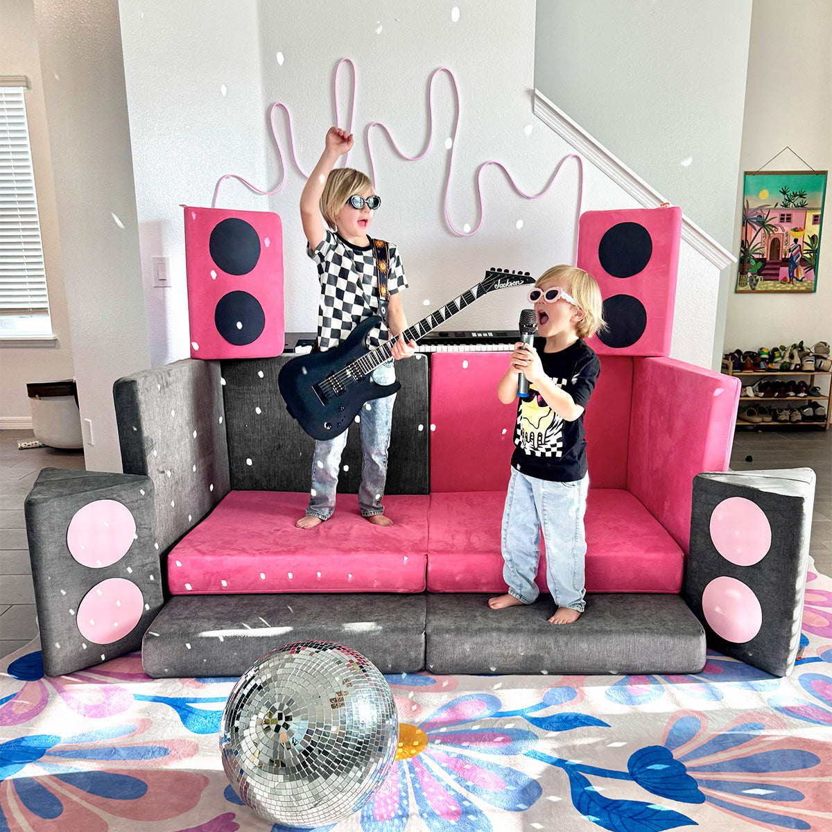 Two kids rock out on a stage built from hot pink and dark gray Nugget play couches.