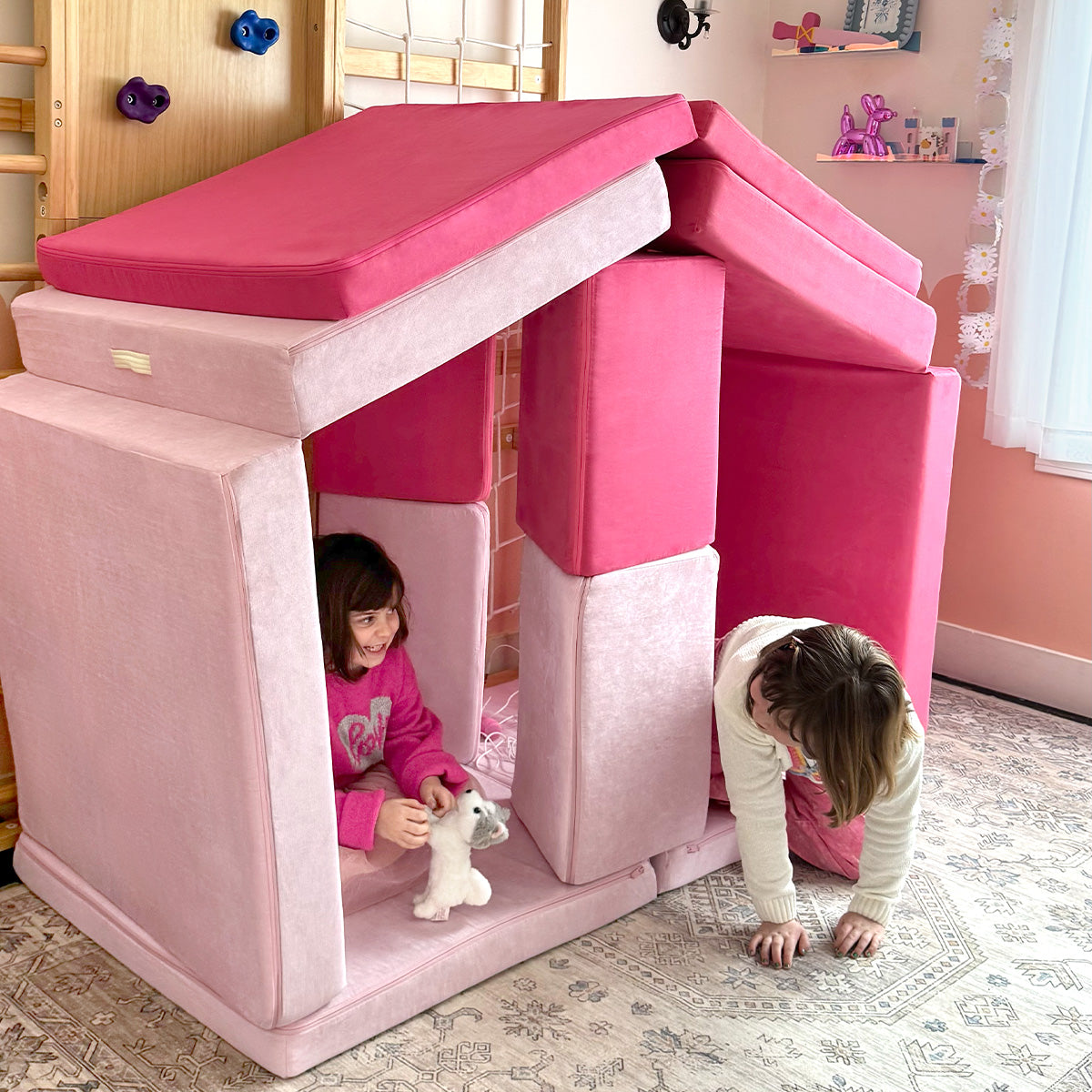 Two girls play in a giant pink Nugget mansion fort built to look like a Barbie dream house.